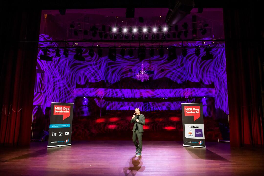 Een man staat op het podium van de grote zaal met mooie lichten op de achtergrond