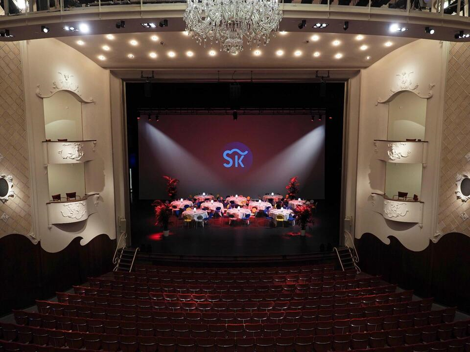 Foto van de grote zaal met stoelen en tafels die op het podium staan