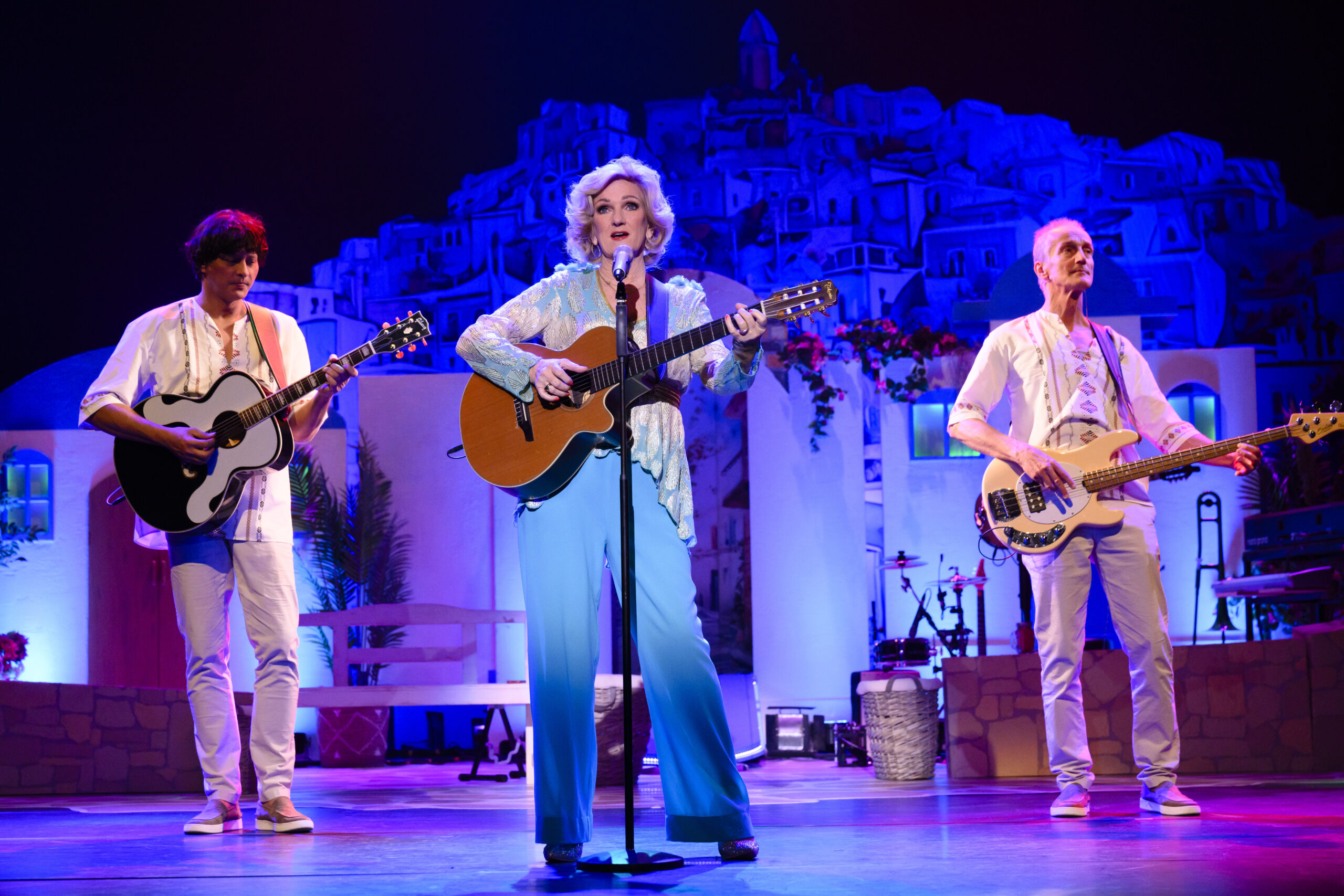 Tineke Schouten staat met een gitaar en twee andere zangers met gitaar te zingen op het podium