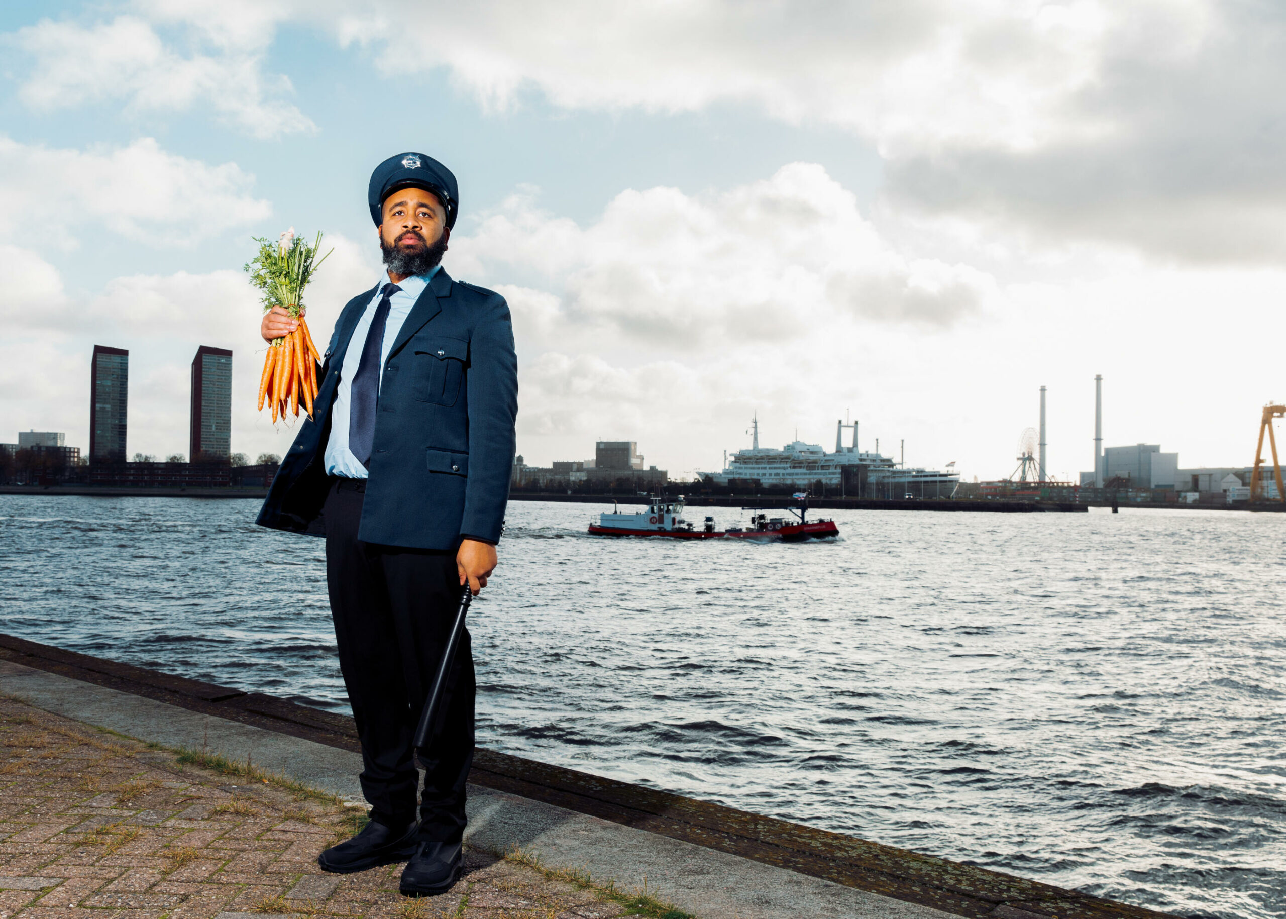 Een agent op de kade met een bos wortels in de hand en op de achtergrond schepen in het water