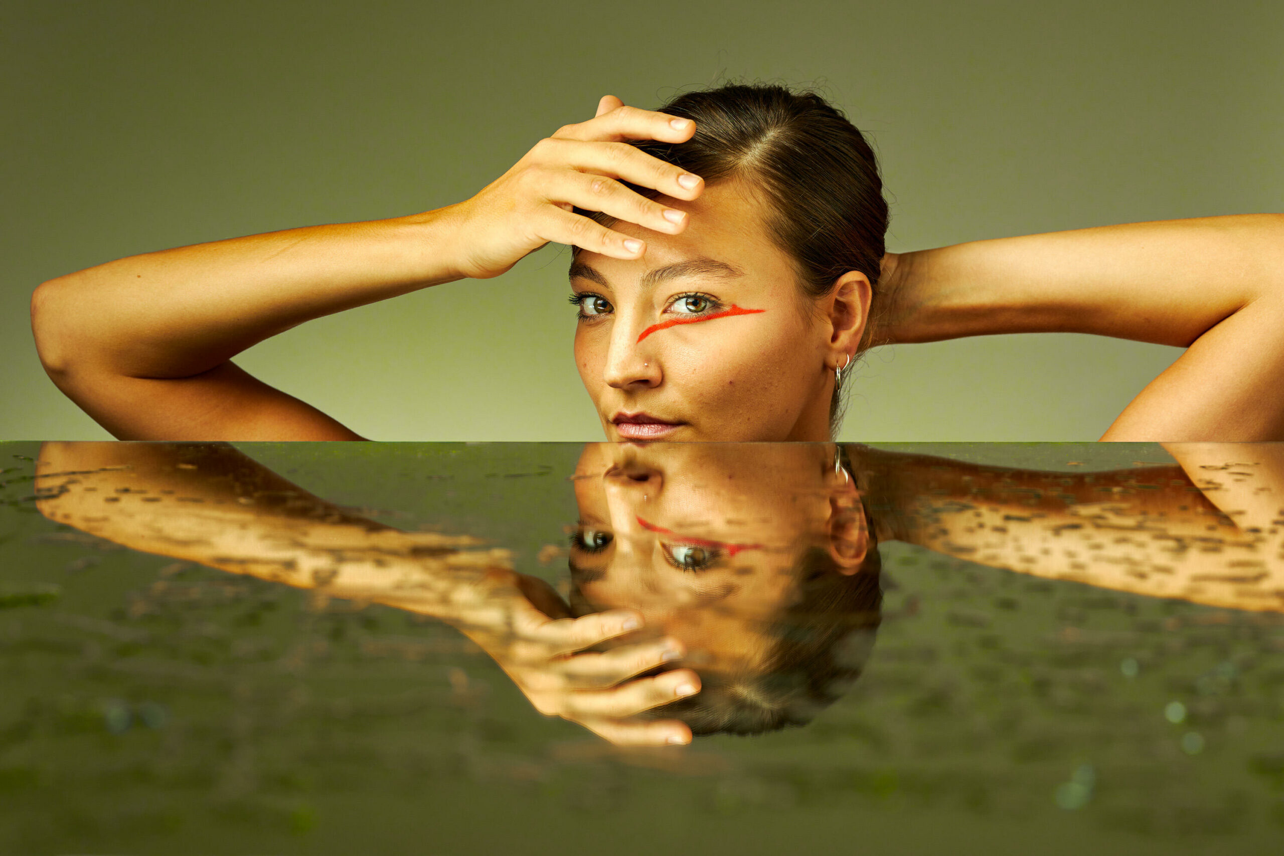 Vrouw met haar armen omhoog en een hand voor het gezicht met daaronder reflecterend water