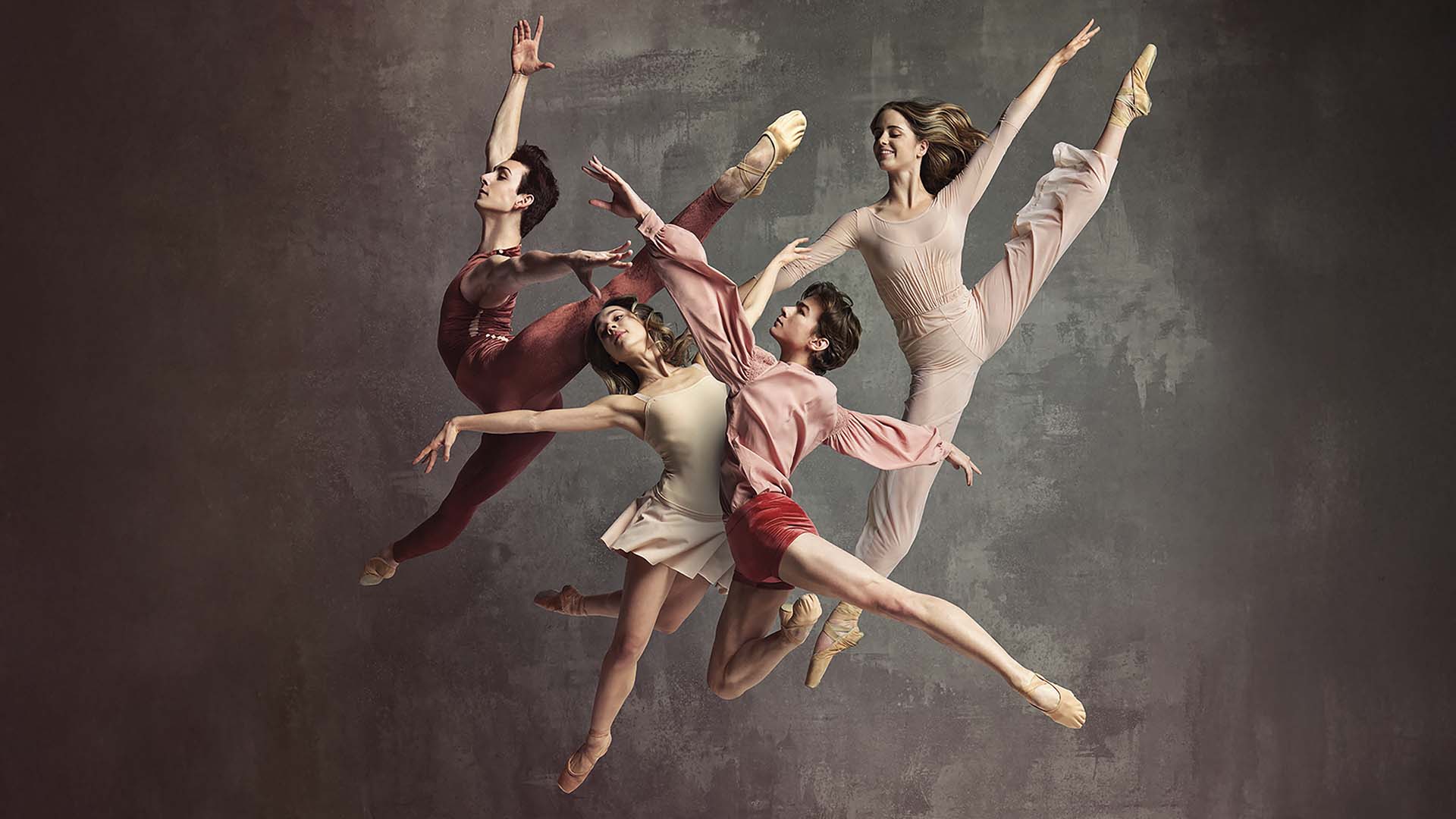 Vijf balletdansers springen sierlijk tegelijk in de lucht tegen een grijze achtergrond.