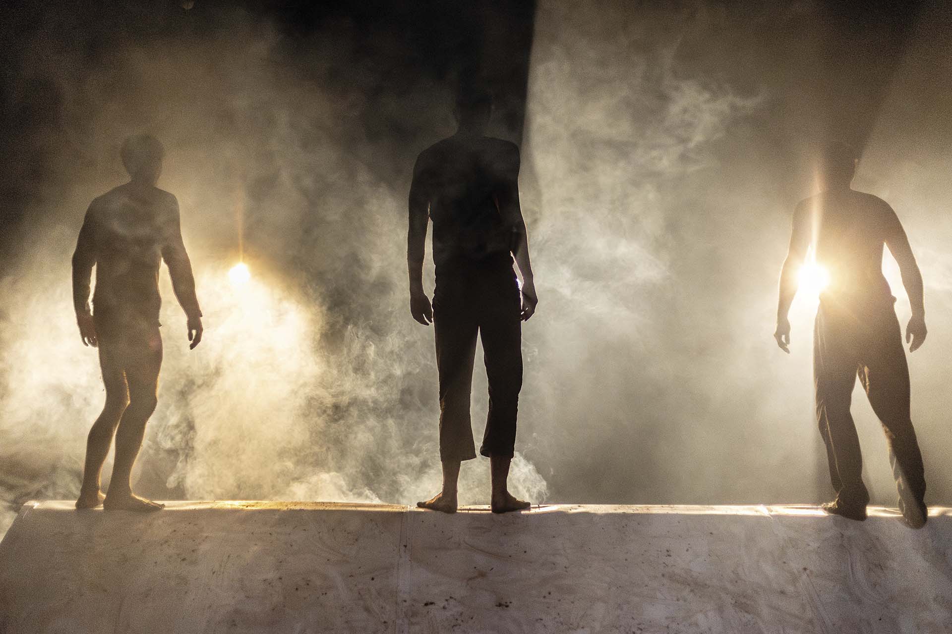 Drie mannen worden van achteren verlicht in een mistige scène met dramatisch tegenlicht.