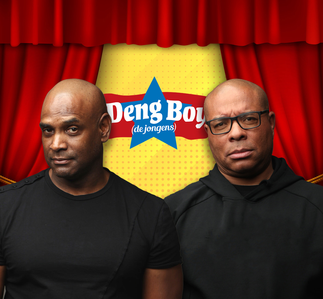 Twee mannen in zwarte kleding poseren voor een rode gordijnachtergrond met in het midden het logo van Deng Boy (de jongens) op een gele ondergrond.