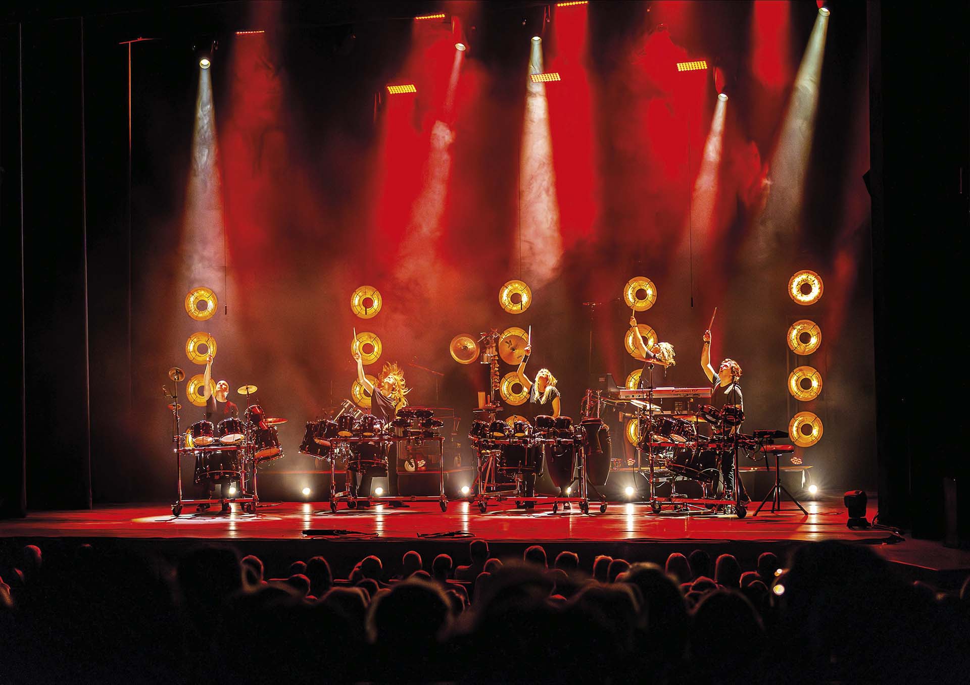 Spectaculaire podiumshow van Slagerij van Kampen met meerdere percussionisten onder rood-geel licht, tijdens de voorstelling Rhythm of Freedom.