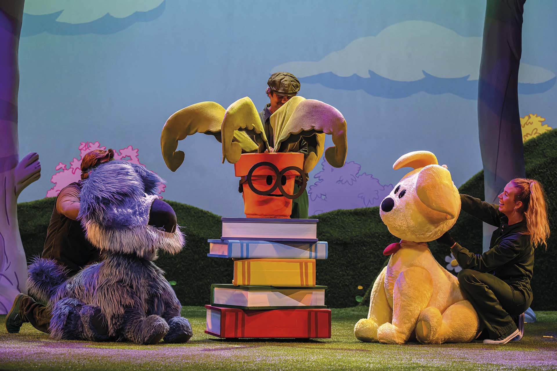 Woezel en Pip staan bij een pratende plant in een bloempot op een stapel boeken in de Tovertuin.