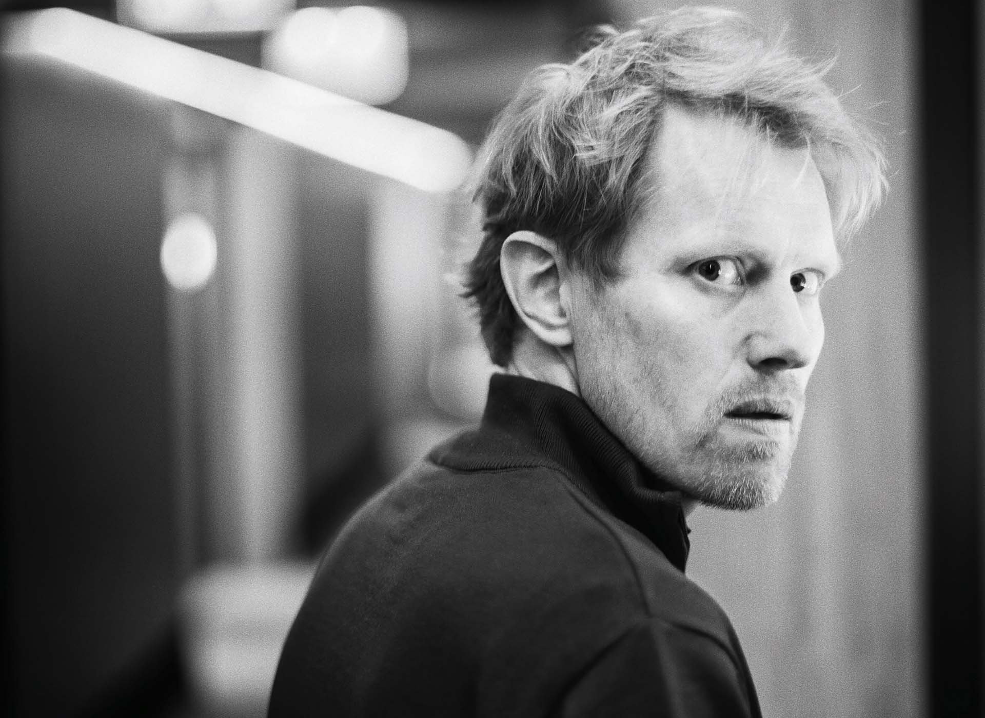 Zwart-wit portret van Jan Beuving die over zijn schouder kijkt met indringende blik in een gangachtige setting