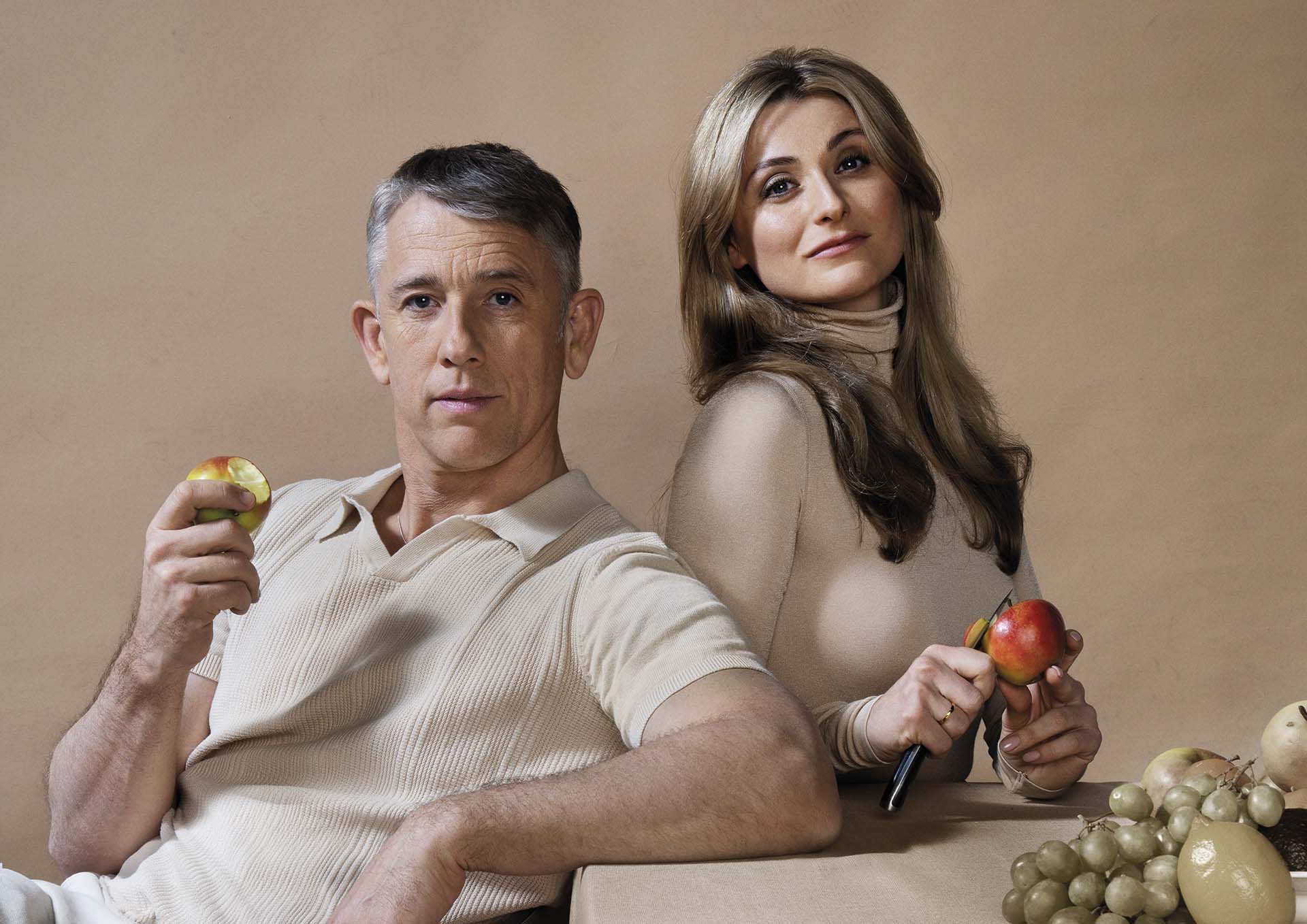Judith Noyons en Waldemar Torenstra zitten naast elkaar en kijken de camera in terwijl ze allebei een appel vasthouden, met fruit op tafel tegen een neutrale achtergrond