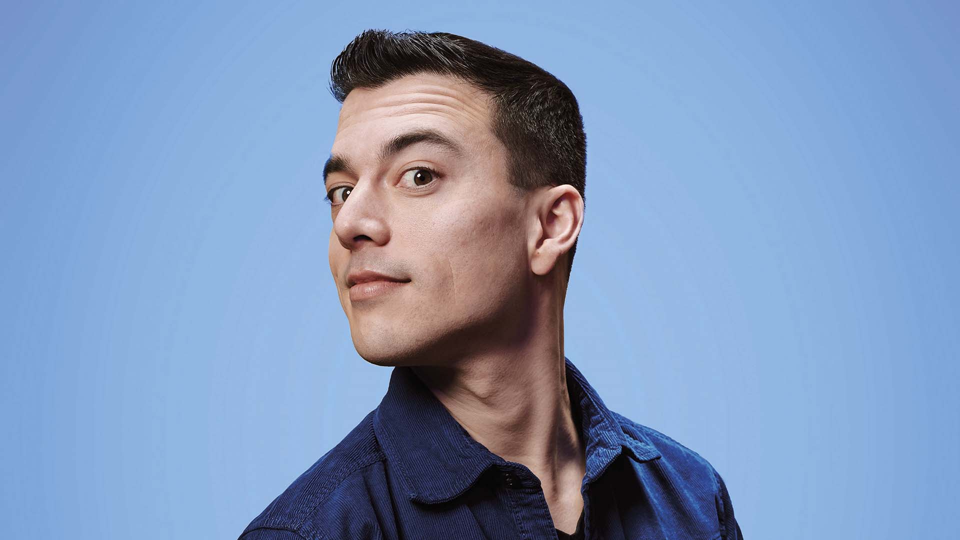 Portret van Andries Tunru tegen een lichtblauwe achtergrond, waarbij hij zijwaarts kijkt.
