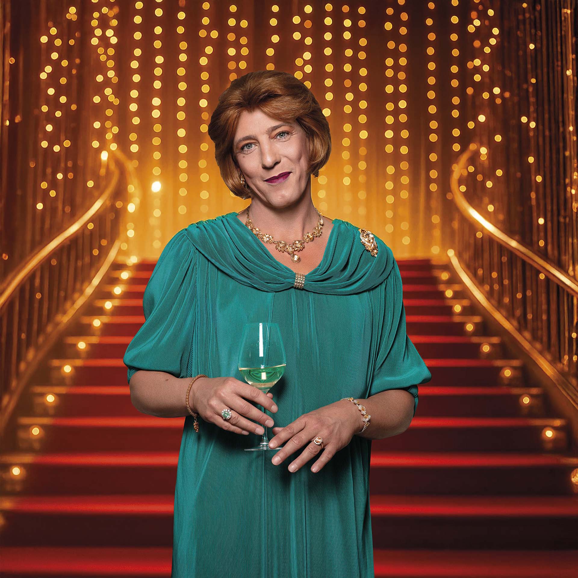 Marja van Katendrecht staat op een verlichte trap met rode treden en gouden lichtjes, gekleed in een groene jurk en met een glas witte wijn in haar hand.