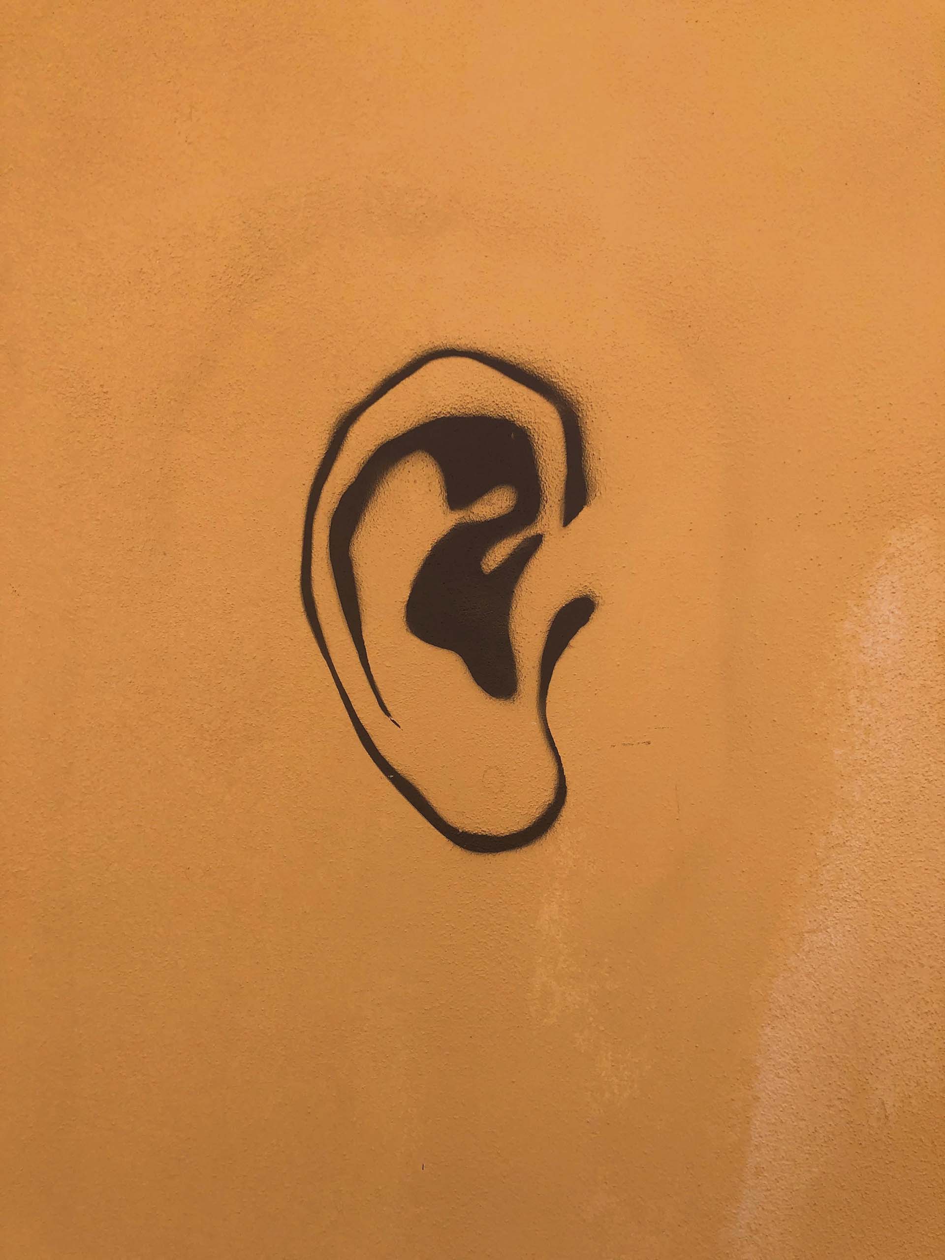 Gestileerde zwarte tekening van een oor op een effen oranje muur