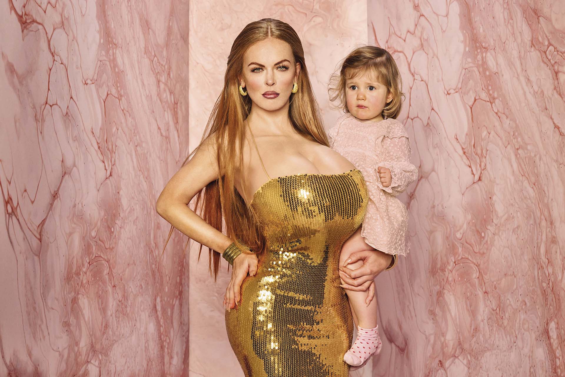 Lisa Ostermann in een gouden jurk met een kind in haar arm. De achtergrond is roze.