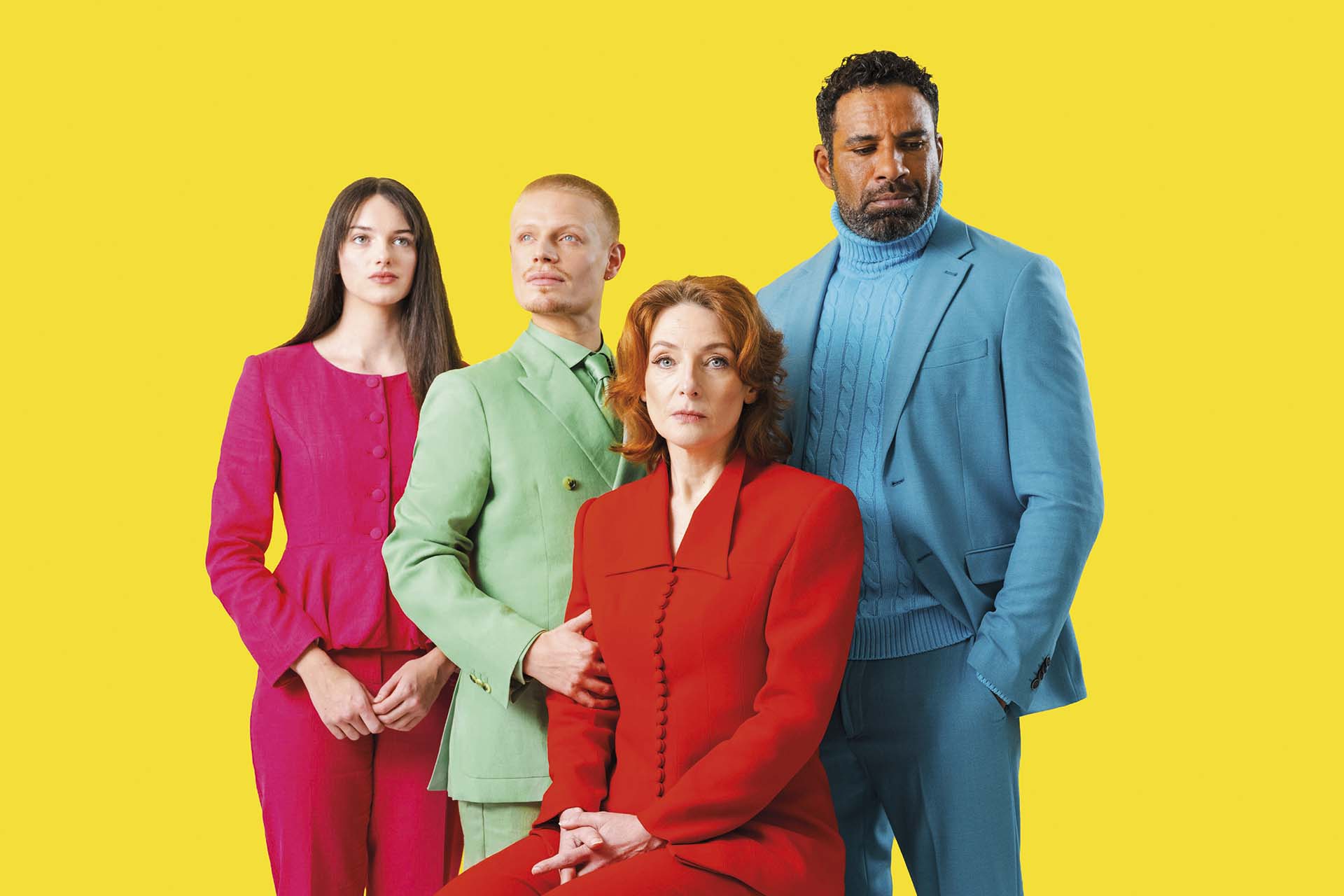 Vier acteurs in opvallende kleurrijke outfits poseren tegen felgele achtergrond, strak en frontaal geportretteerd in gestileerde groepsopstelling