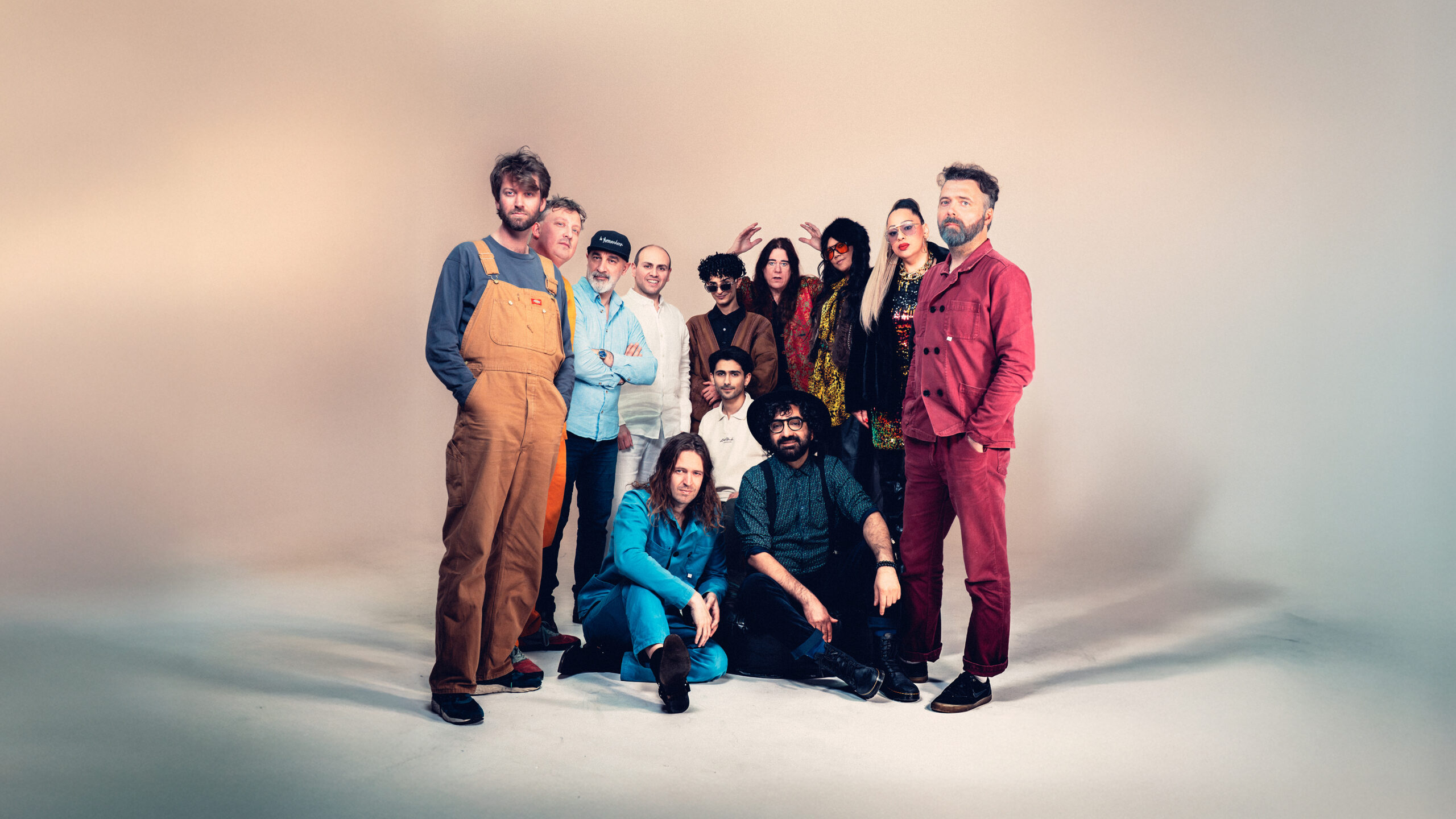 Groepsfoto van de band De Niemanders met elf muzikanten in kleurrijke kleding tegen een neutrale studioachtergrond