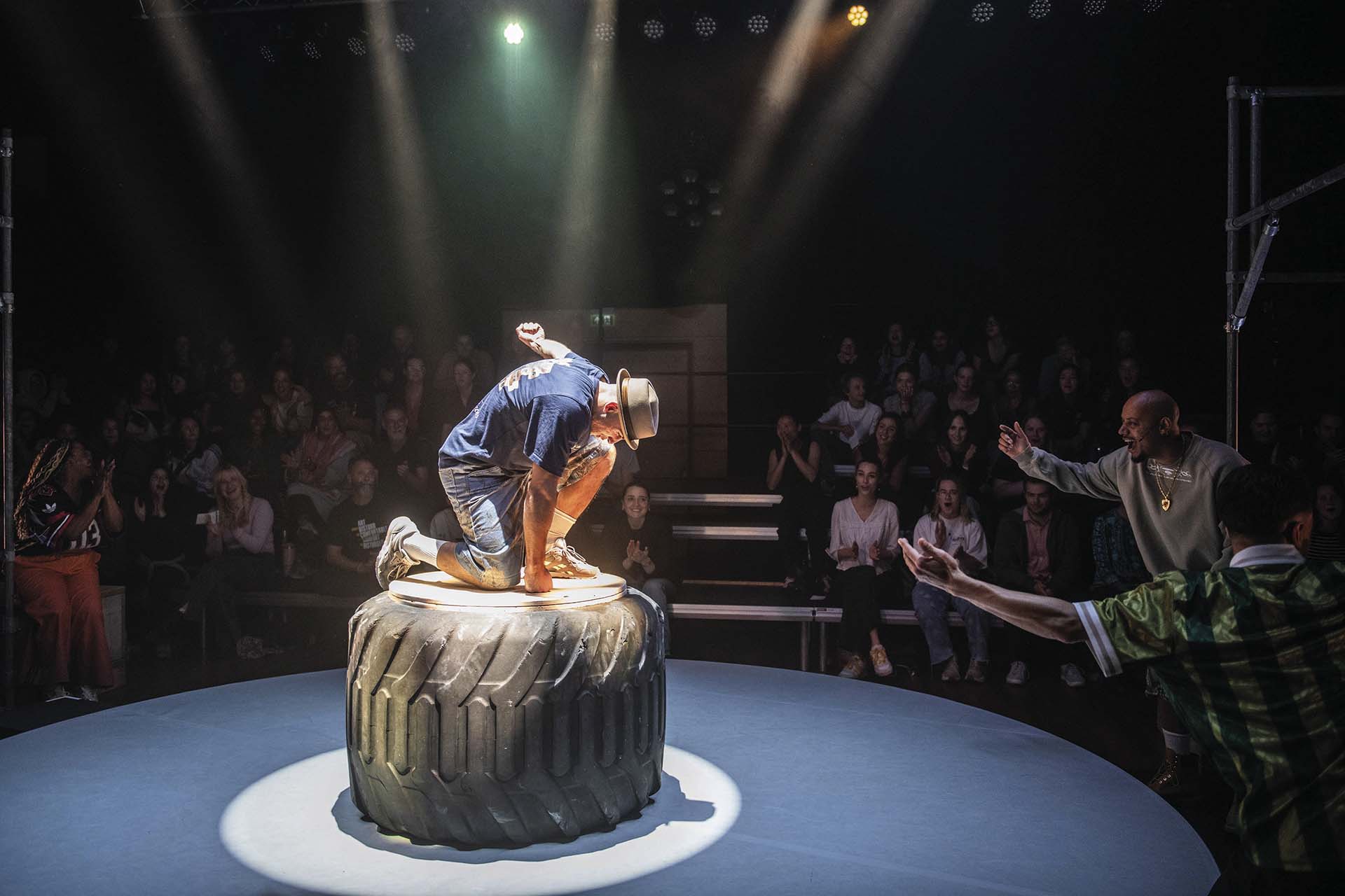 Danser landt geknield op bandvormig podium, publiek applaudisseert