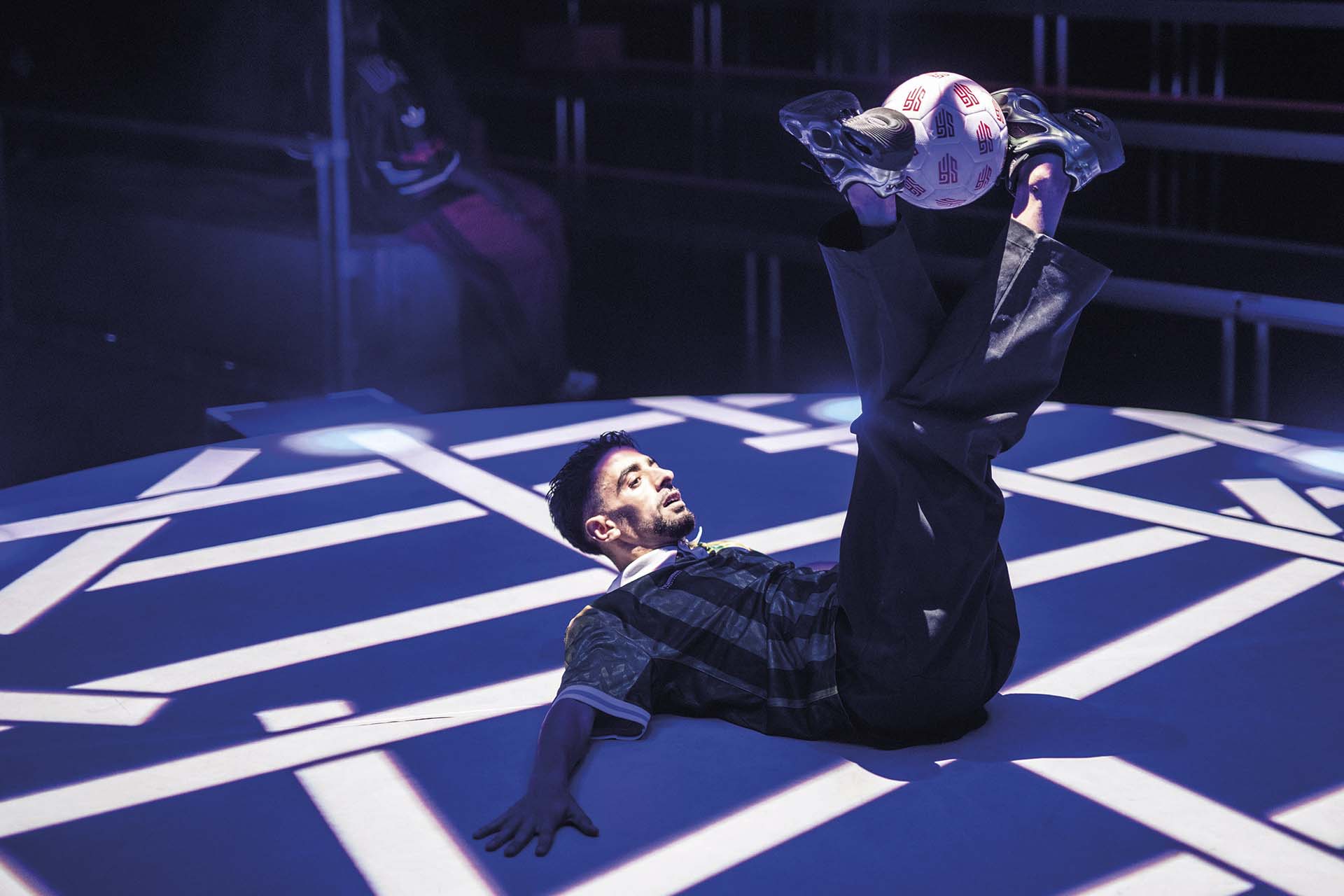 Danser balanceert voetbal liggend op rug onder blauwe spots
